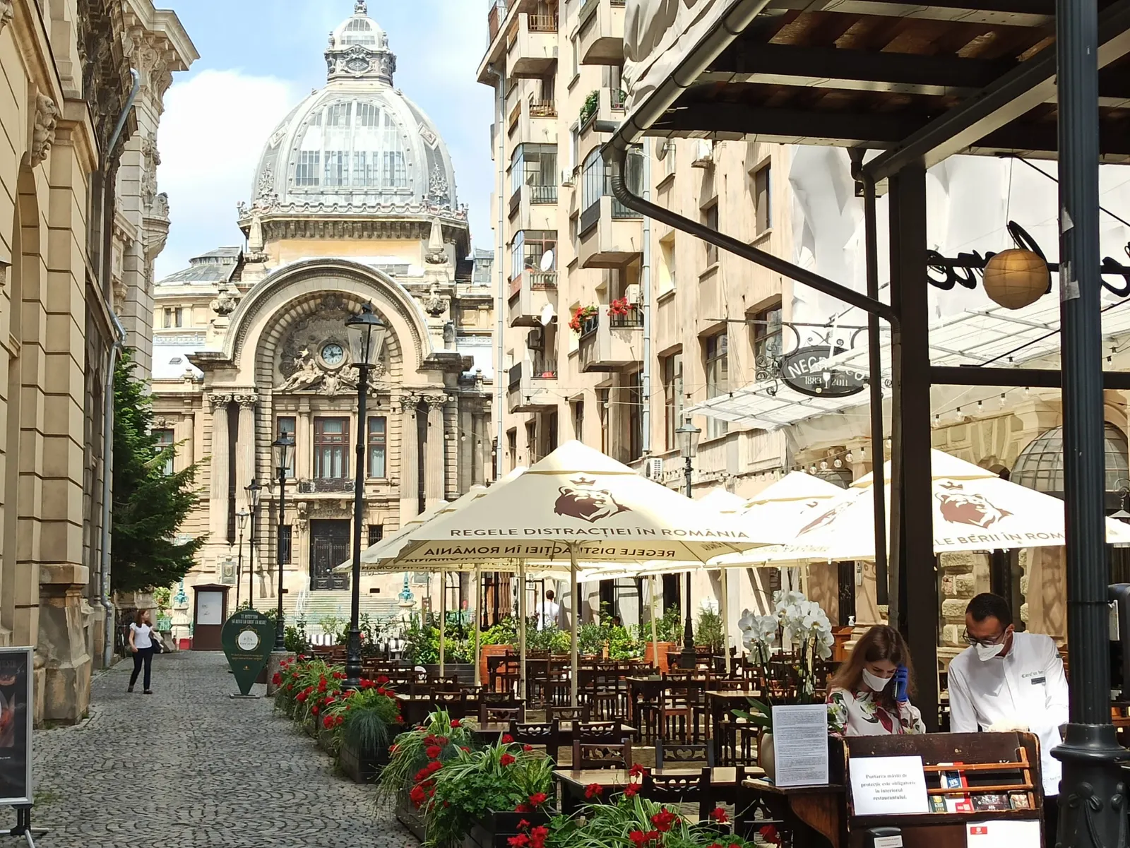 Café terraces on a cobbled Old Town street facing the CEC Palace in Bucharest