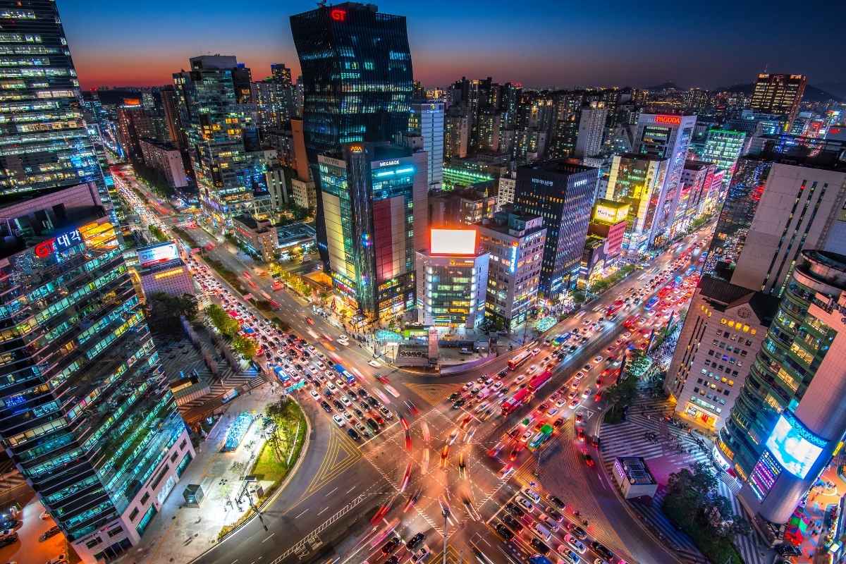 Seoul at dusk from above, with neon-lit towers and light trails across a busy intersection